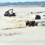 A heavy machine operator loads mud onto a tractor trolley along the banks of the Indus River