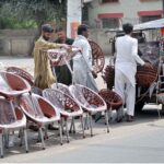 A vendor is busy arranging and displaying plastic-made chairs to attract the customers at his roadside setup