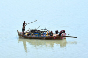 A heavy machine operator loads mud onto a tractor trolley along the banks of the Indus River