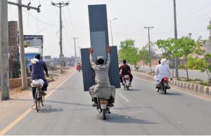 A person holding a huge mirror while sitting on the rear seat of motorcycle