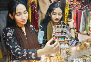 Girls select and purchase artificial jewelry from a vendor stall as part of Eid ul Fitr shopping at a local market
