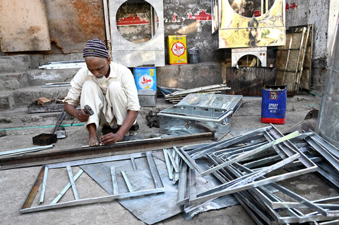 An aged man is preparing a room cooler frame at his workplace in the city