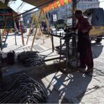 A worker skillfully bends iron pipes outside his shop to make chairs