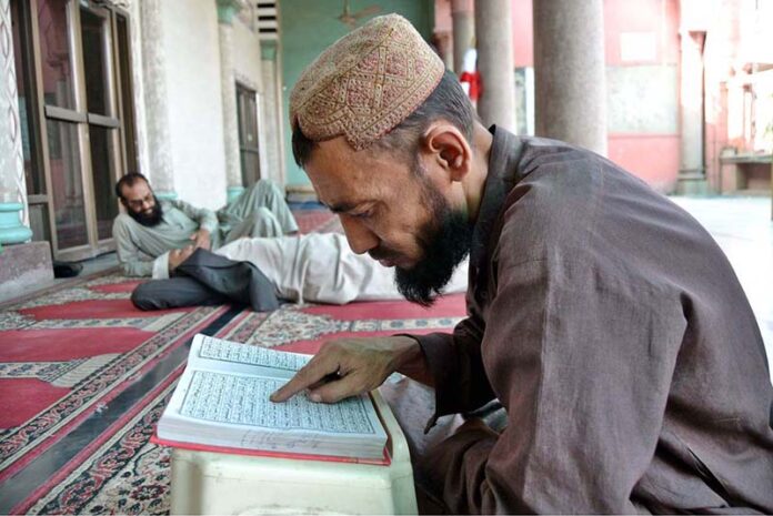 A person is engrossed in reciting the Holy Quran in Jamia Masjid Noori during holy fasting month of Ramadan