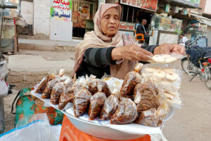 An aged woman displays food items to sell for livelihood at her roadside setup during the Islamic fasting month of Ramadan ul-Mubarak in the City