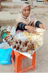 An aged woman displays food items to sell for livelihood at her roadside setup during the Islamic fasting month of Ramadan ul-Mubarak in the City