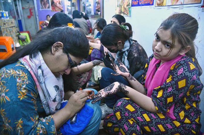 Artisans applies henna (mehndi) to girls’ hands as they prepare for Eidul Fitr celebrations at Meena Bazaar