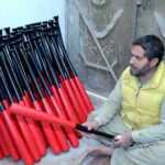 A worker is making final adjustments to a baseball bat at a local sports factory