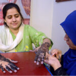 A woman applying Hinna (Mehndi) to a journalist family member in ‘Mehndi Night’ organized by Karachi Press Club (KPC)
