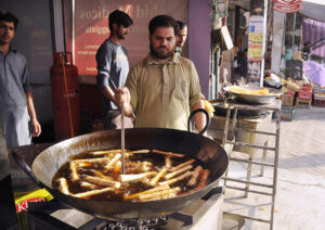 A seller of Chicken and Vegetable rolls in a local bazaar near Shadman town in the holy month of Ramadan frying the Chicken and Vegetable rolls in oil