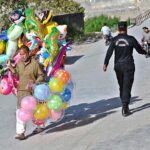 An elderly man strolls through a street in the capital, carrying balloons to earn a livelihood for his family