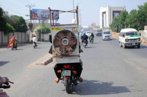 A person holding a room cooler while sitting on the rear seat of a motorcycle.