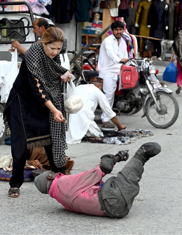 A woman gives mercy to a beggar crawling on the road at Bara Bazar