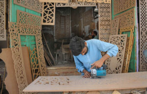 A worker is busy carving a design on the wooden sheet with the help of a machine at his workplace.