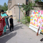 A woman experiences to shot balloons with a pallet gun during their visit to Lok Virsa on the second day of Eidul Fitr celebrations in the federal capital