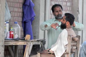A local barber trims a customer’s beard at his roadside stall—one of many street barbers offering affordable services to daily wage workers and locals despite limited resources.
