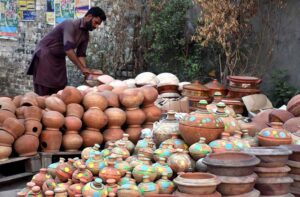 A vendor arranging and displaying the different kinds of clay pots to attract the customers at roadside setup.