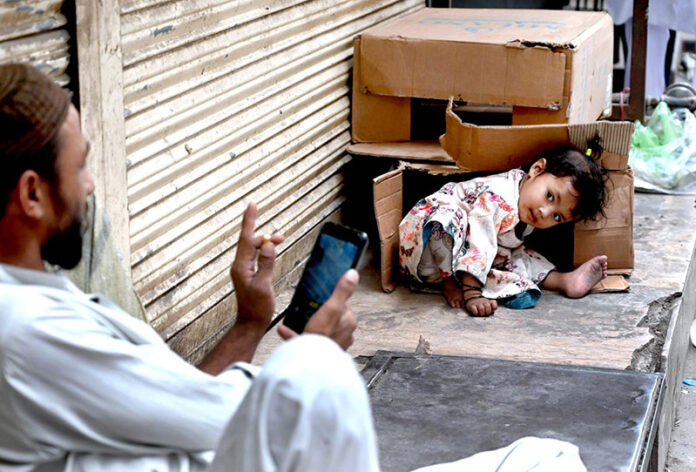 A minor girl playing on the footpath while her father capturing the moment in his cell phone