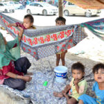 A gypsy mother gently swings her child in a makeshift hammock tied to a tree on the outskirts of Qasimabad
