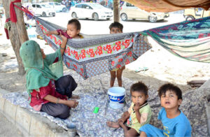 A gypsy mother gently swings her child in a makeshift hammock tied to a tree on the outskirts of Qasimabad