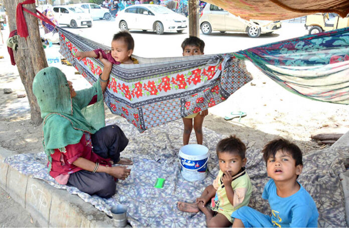 A gypsy mother gently swings her child in a makeshift hammock tied to a tree on the outskirts of Qasimabad