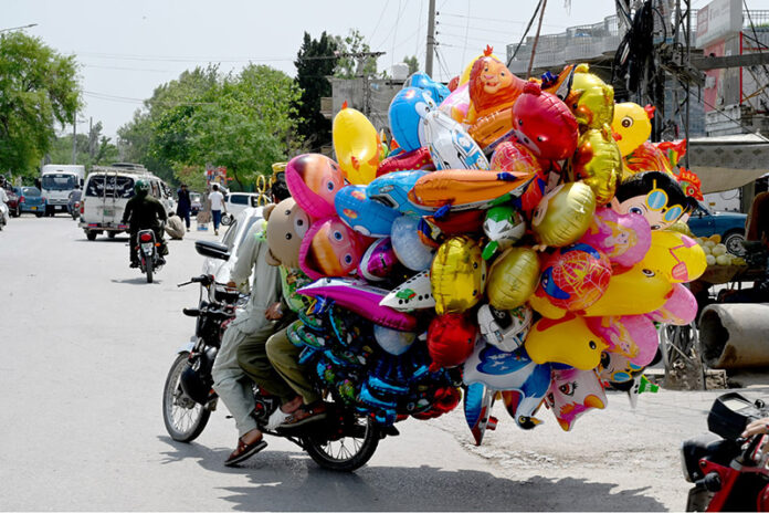 A pillion rider carrying colourful balloons to sell for livelihood