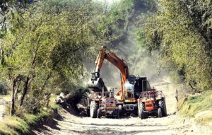 A view of an excavator and tractor cleaning local water canal to improve agricultural water supply