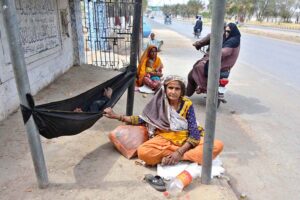 A woman swings her baby in a piece of cloth tied to pipe on the footpath outside the Cantt graveyard.
