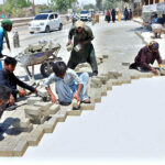 Labourers are busy fixing cemented tiles during construction work of road at Qasimabad