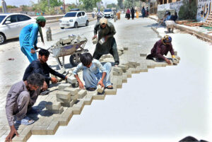 Labourers are busy fixing cemented tiles during construction work of road at Qasimabad