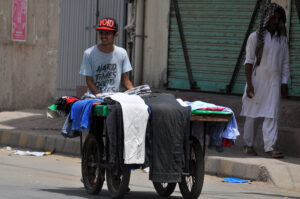 A young street vendor displaying and selling used clothing at affordable prices, striving to support his family.