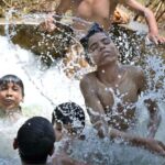 Youngsters enjoying bathing in the running tube-well to get relief from hot weather in the city