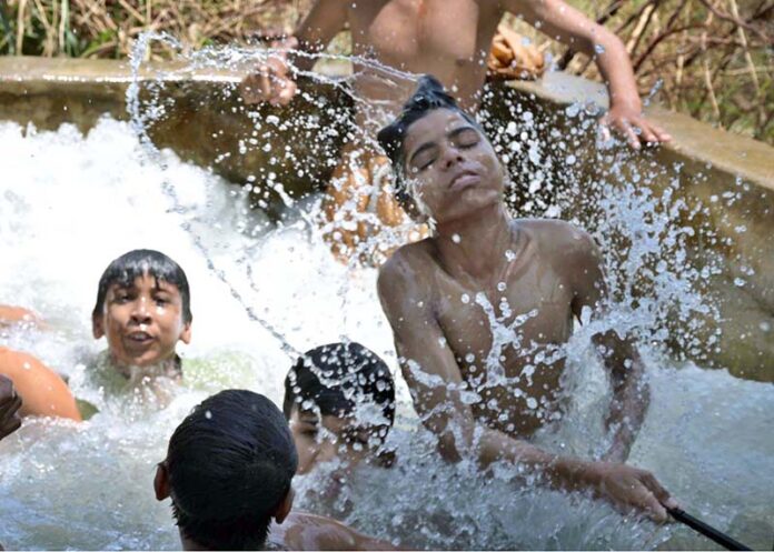 Youngsters enjoying bathing in the running tube-well to get relief from hot weather in the city