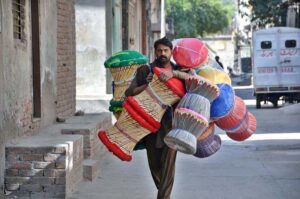 A street vendor carries handmade bamboo cane stools on his shoulder, strolling through the streets of the twin cities to earn an honest livelihood for his family.
