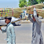 Street vendors carrying brooms on their head to sell while strolling through the streets of Latifabad in the city