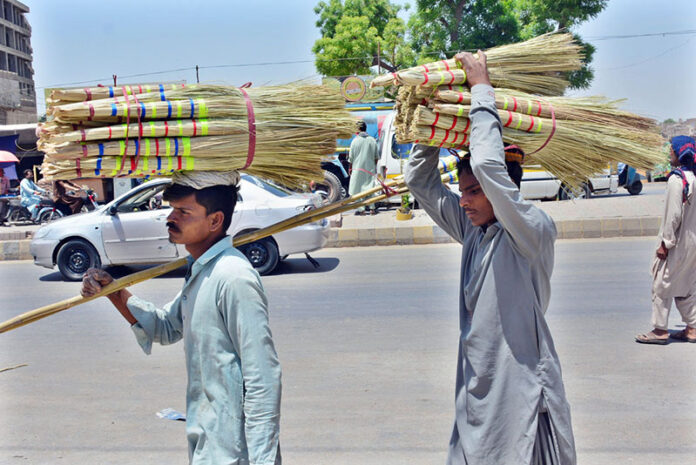 Street vendors carrying brooms on their head to sell while strolling through the streets of Latifabad in the city