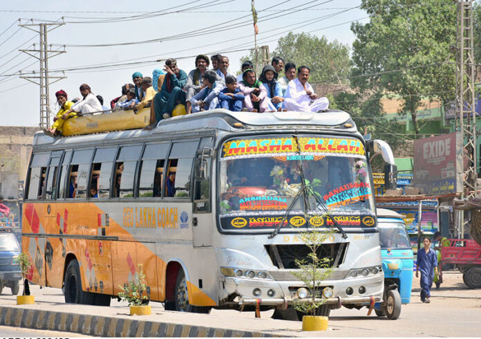 Passengers travel on the rooftop of a bus along Jail Road, in violation of traffic laws, posing a serious safety risk