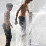 Young boys beat the heat by enjoying a playful shower from a leaking water pipeline over the canal in the city