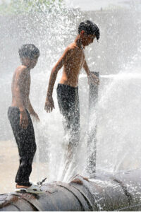 Young boys beat the heat by enjoying a playful shower from a leaking water pipeline over the canal in the city