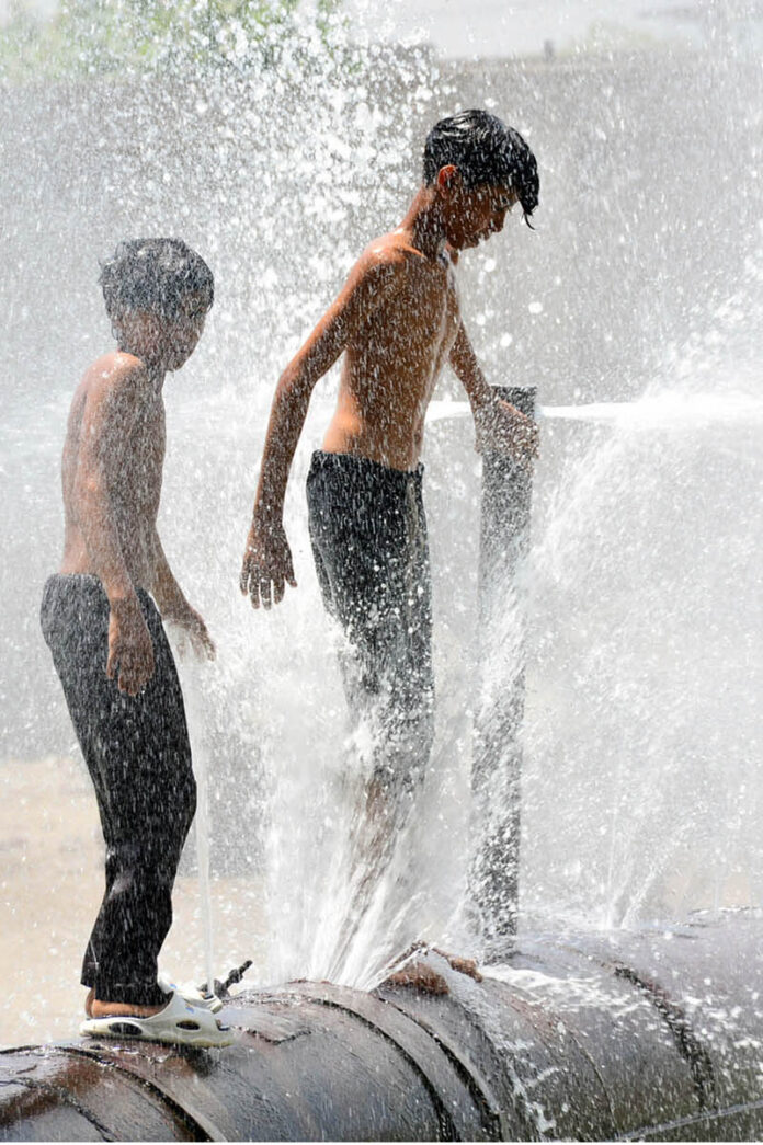 Young boys beat the heat by enjoying a playful shower from a leaking water pipeline over the canal in the city
