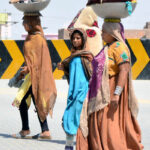 Nomadic women carry bundles of clothes on their heads as they walk toward the canal for washing, far from their homes in the Hala Naka area