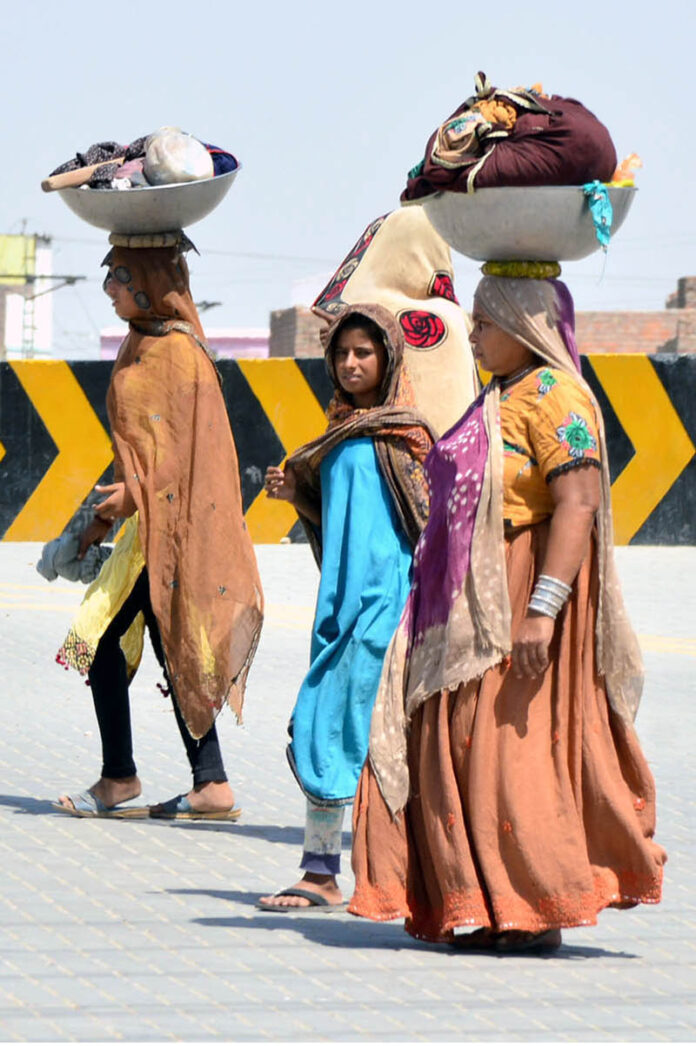 Nomadic women carry bundles of clothes on their heads as they walk toward the canal for washing, far from their homes in the Hala Naka area
