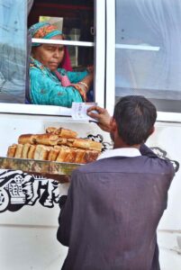 Vendor selling traditional food item Aloo petis to a woman in a local bus at Tando Yousuf Area.