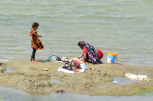 A nomadic woman with her daughter wash clothes along the Indus River at Hussainabad.