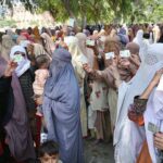 Women show their ID cards while waiting for their turn at a BISP cash distribution point at Government No.1 School, GT Road in provincial capital