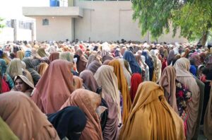 Women show their ID cards while waiting for their turn at a BISP cash distribution point at Government No.1 School, GT Road in provincial capital