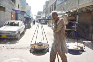 An elderly vendor sells roasted grams while shuttling along the road in the Korangi area to attract customers.