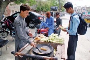 A Young vendor preparing and selling roasted corn cob at roadside.