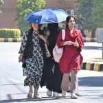 Students shield themselves from the sun with umbrellas while walking through the campus of Sargodha University