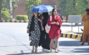 Students shield themselves from the sun with umbrellas while walking through the campus of Sargodha University